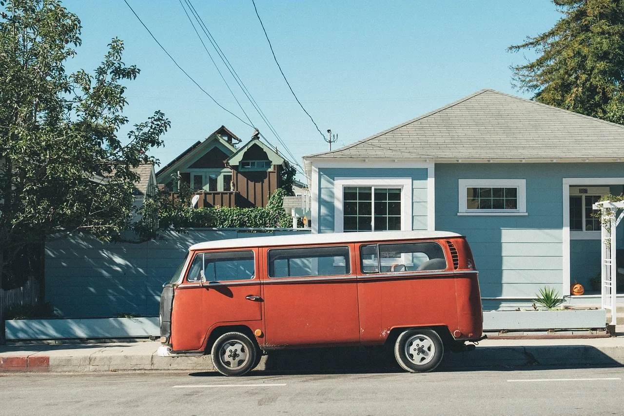 An old van parked at the curb in front of a small house