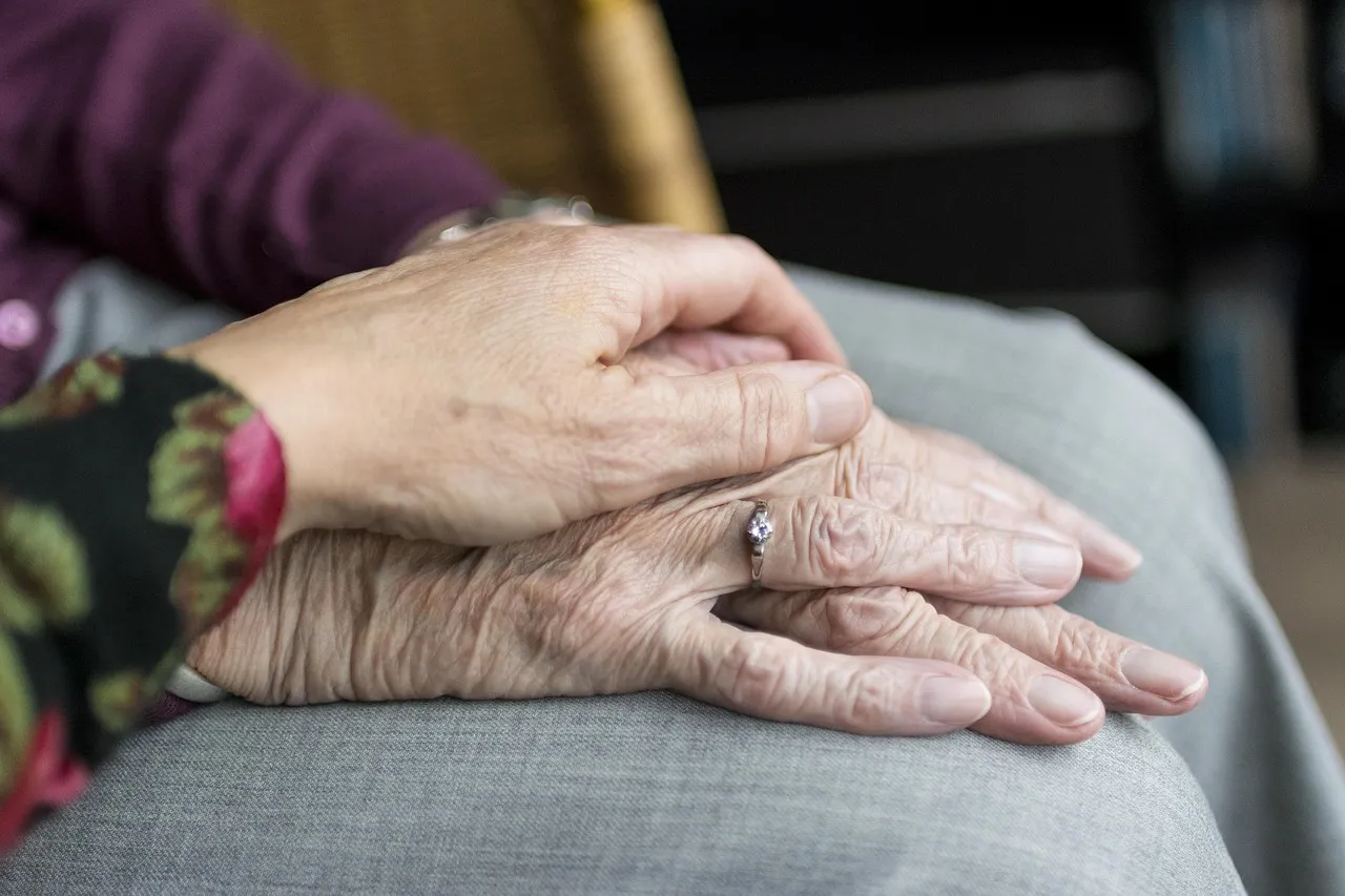 A younger hand resting gently on an elderly woman's folded hands