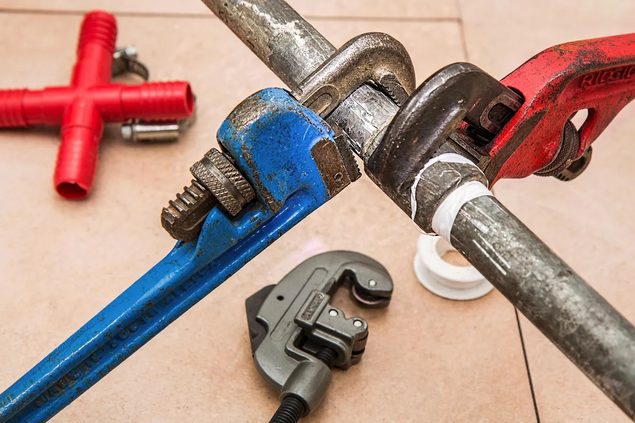 Two pipe wrenches clamped on a length of galvanized pipe, with a tube cutter beside them